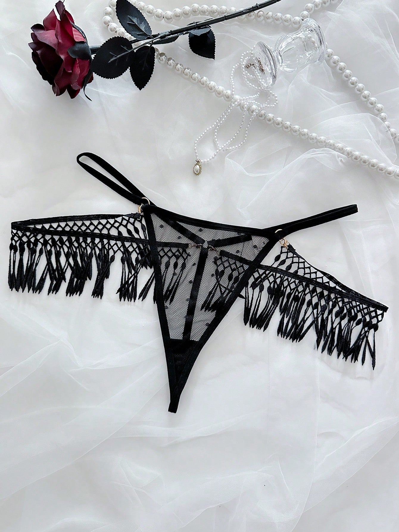 Women's black low-rise thong panties with mesh panel detail, cut-out design, and fringe accents in knitted stretch fabric.