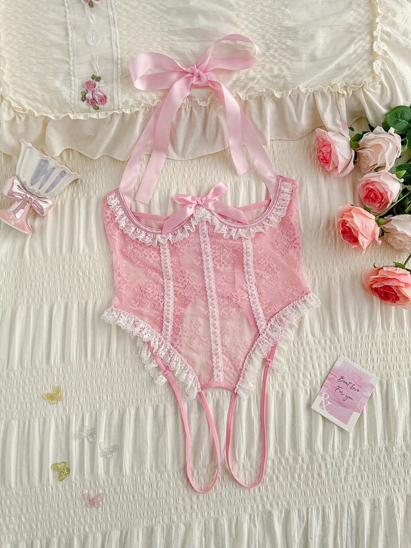 Pink lace lingerie jumpsuit for women with halter neckline, backless design, adjustable straps, ruffle hem, semi-sheer fabric, and thong bottom.