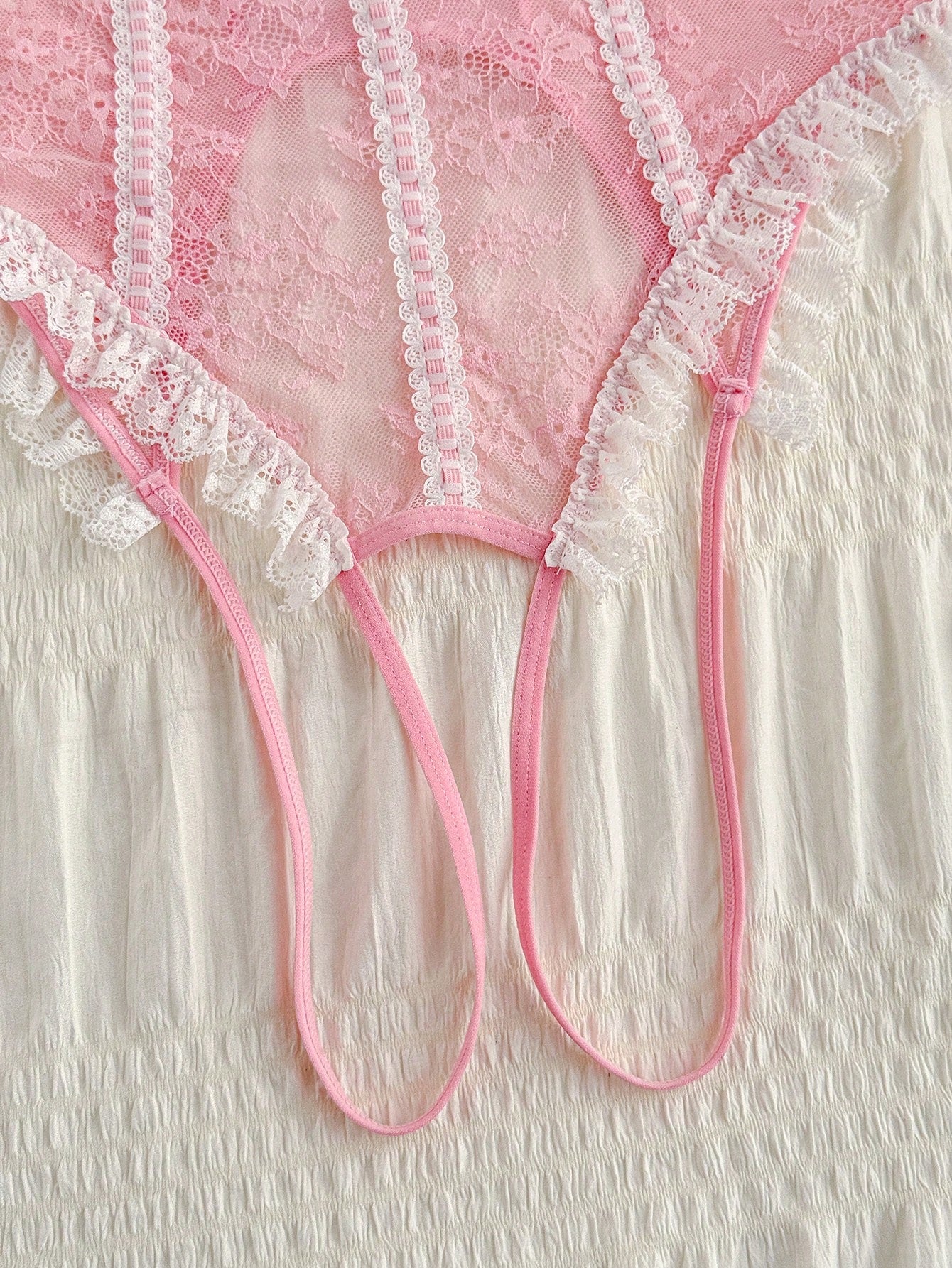 Pink lace lingerie jumpsuit for women with halter neckline, backless design, adjustable straps, ruffle hem, semi-sheer fabric, and thong bottom.